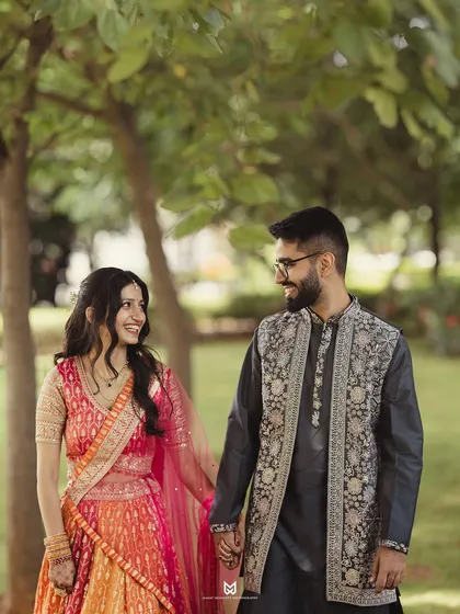 A candid shot of a couple walking hand in hand during their Roka ceremony. The natural park setting provides a beautiful, soft backdrop.