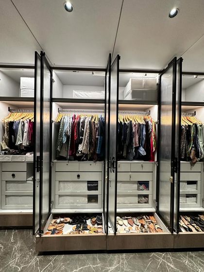 A full view of a stunning, organized walk-in closet. With fluted glass doors and internal lighting, every section is a perfectly curated display of clothes, shoes, and accessories.