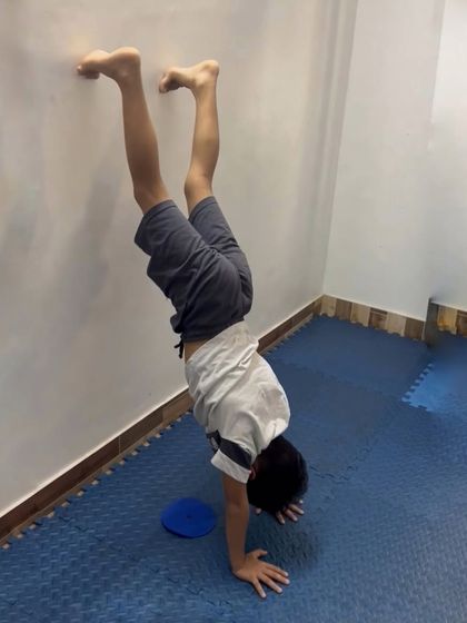 A student practices a wall-assisted handstand, an excellent exercise for building upper body strength and confidence.