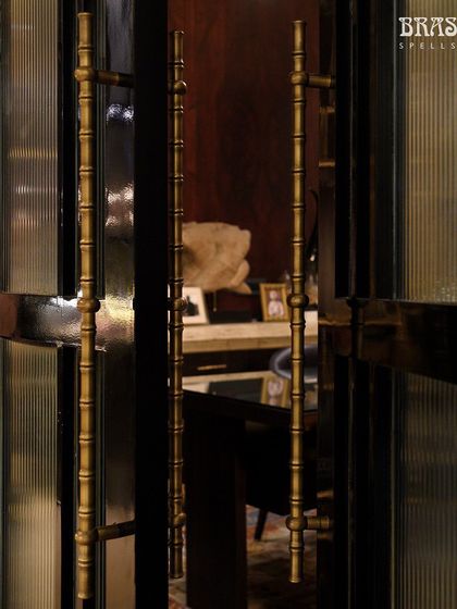 A closer look at the Bamboo door pulls at the JJ Valaya store. The Antique Brass finish provides a warm contrast to the dark door frame, highlighting the handle's texture and form.