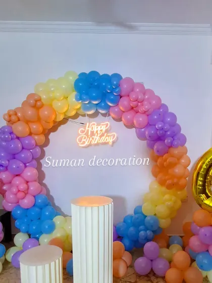 This colorful unicorn and rainbow-themed decoration for a 6th birthday includes a full ring of pastel balloons, a "Happy Birthday" neon sign, and a unicorn balloon column.