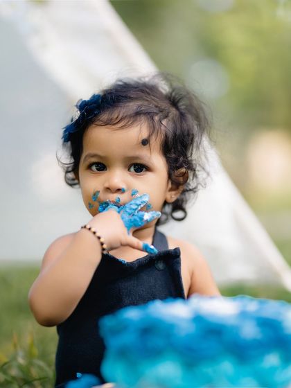 A close-up of the birthday girl getting her hands delightfully messy with blue cake frosting. This shot focuses on the tactile, fun aspect of a cake smash.