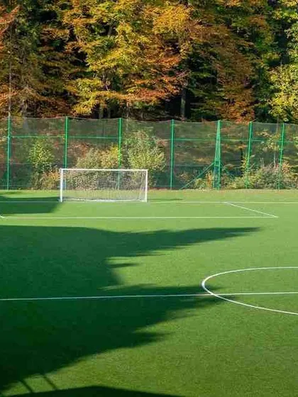 Our artificial turf fields can be seamlessly integrated into any environment. This installation shows a full-size pitch with clear markings, surrounded by trees, providing a beautiful and functional sporting space.