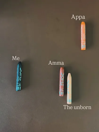 The tools for discovery can be very simple. Here, crayons represent different members of a family system, including 'Me', 'Amma', 'Appa', and the acknowledged presence of 'The unborn'. This constellation work helps bring light to all parts of a family story, honoring every member and experience to restore balance.