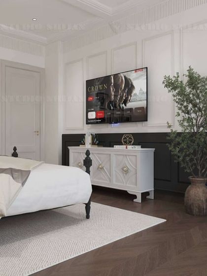 The TV is mounted on a wall with classic molding, opposite the bed, with a vintage-style console table below.