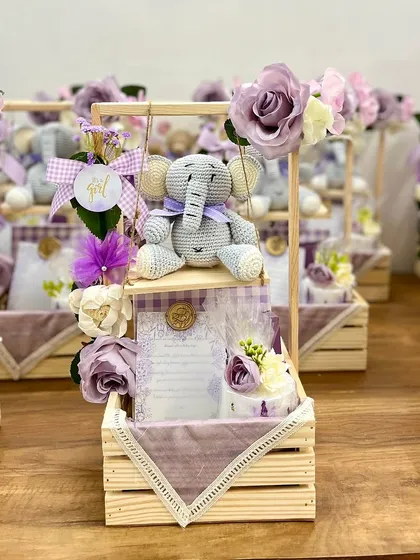 Announcing the arrival of a precious baby girl with these enchanting hampers. Centered around a sweet, handcrafted crochet elephant on a swing, these gifts are curated with a soft lavender palette, personalized notes, and delicate floral touches for a truly heartwarming reveal.