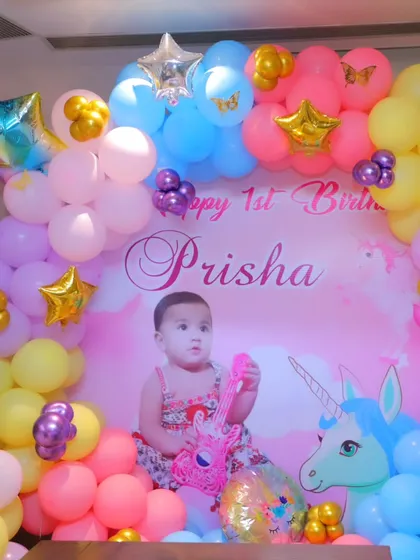 A close-up of a first birthday backdrop with a custom print of the baby girl, surrounded by a vibrant multi-colored balloon arch with unicorn elements.