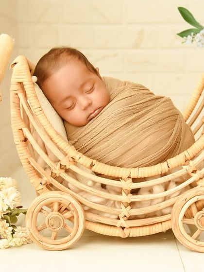 A close-up of a baby sleeping peacefully in a wicker pram, framed by soft greenery. This highlights the calm and serene nature of my rustic setups.