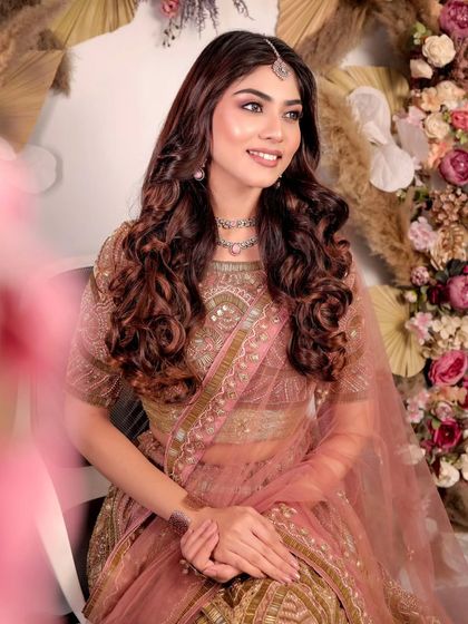A smiling portrait of a model in the dusty pink and gold lehenga. The soft curls and delicate jewellery create a romantic look perfect for an engagement photoshoot.