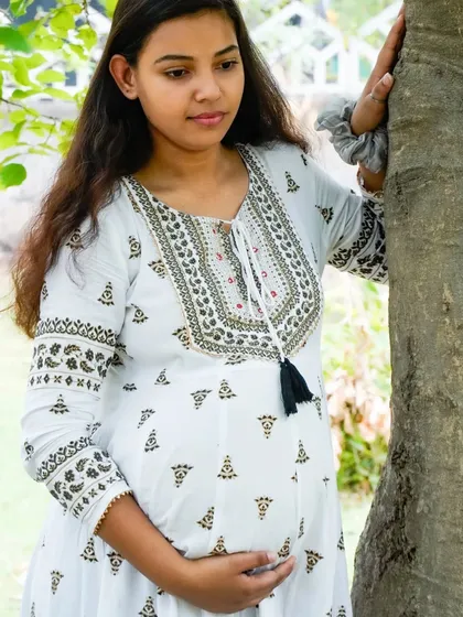 A candid shot of an expecting mother looking thoughtful while leaning against a tree. Our outdoor maternity sessions include a mix of posed and natural moments.