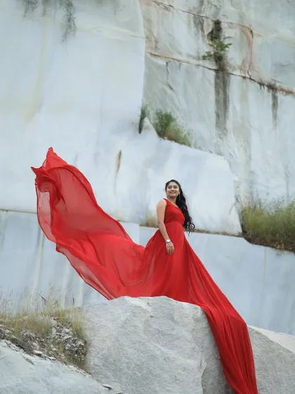 A solo portrait that commands attention. The fiery red train of this gown cascades down the rocks, creating a powerful and artistic statement for a portfolio or pre-wedding shoot.