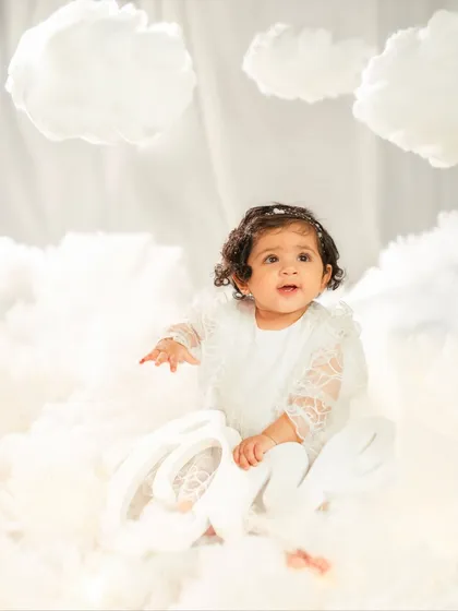 Another angle of the birthday girl holding her "One" sign, showing off the beautiful details of her lace dress and the fluffy cloud props.