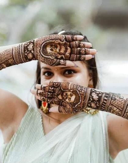 A professional shot of a bride showcasing her stunning portrait mehendi. The design features intricate portraits of the couple on both palms, a true centerpiece for her bridal look.