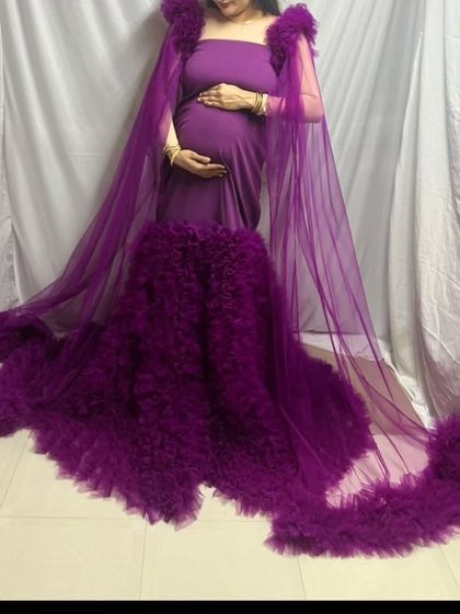 A full view of the dramatic purple maternity gown with its ruffled shoulder details and flowing cape. This is a perfect rental for creating high-impact, fashionable maternity portraits.
