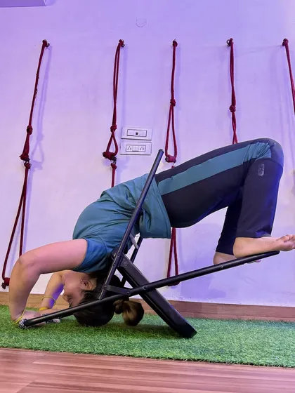 A different perspective of the chair-supported headstand, showing the engagement of the core and legs.