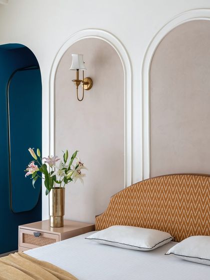 Arches and soft textures define this serene master bedroom. We created arched panels behind the bed in a gentle beige lime plaster finish, complemented by a woven headboard and a classic brass wall sconce for a touch of elegance.