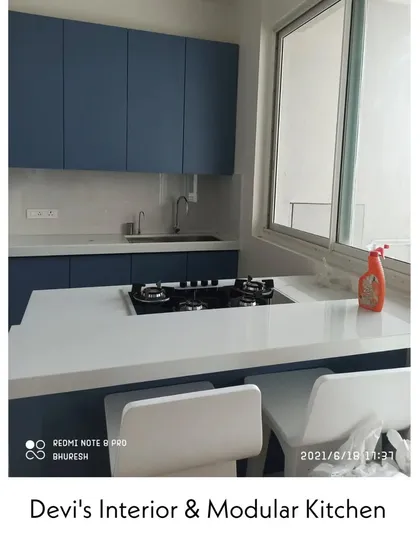 A simple and elegant kitchen in Andheri with matte blue cabinets and a clean white countertop that doubles as a breakfast bar. The large window provides excellent ventilation and natural light.