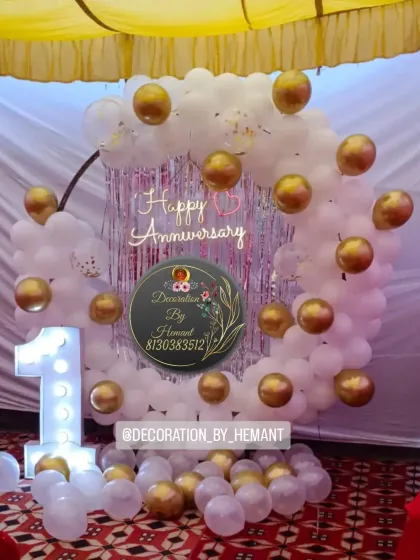 A dreamy first-anniversary decoration. The setup includes a ring backdrop made of white balloons with gold chrome accents, a lit-up number '1', and a "Happy Anniversary" sign.