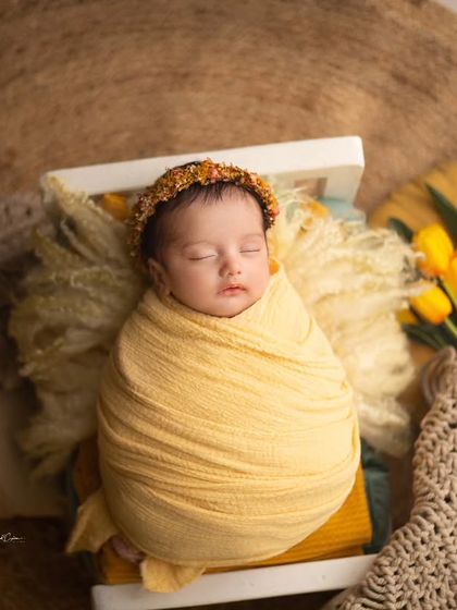 A beautiful overhead shot of a baby girl swaddled in a tiny bed. The warm yellow wrap and natural textures create a sunny and cheerful feel.