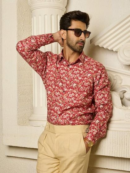 The red floral shirt, paired with light beige trousers, creates a balanced and stylish ensemble that is perfect for a sunny day or a casual evening out.