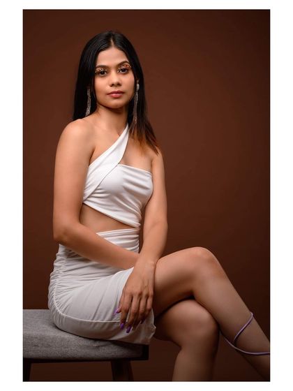 A seated studio portrait in a stylish white dress. The pose is elegant and relaxed, creating a sophisticated fashion shot.