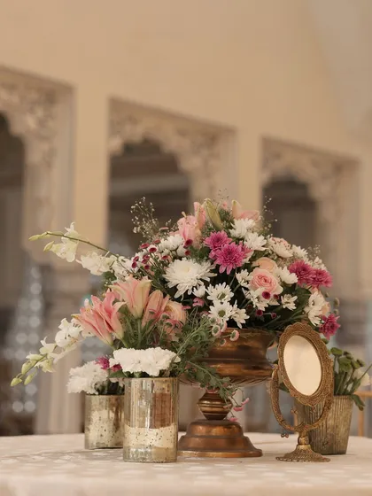 A simple yet elegant centerpiece for the lunch tables, featuring a mix of pastel flowers in a golden vase, accompanied by a small vintage-style mirror.