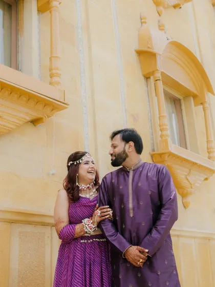 A happy, candid moment during a shoot at a palace hotel in Jaisalmer. The couple's coordinated purple outfits look stunning against the golden sandstone architecture.