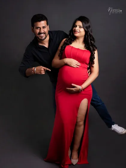 A playful and fun pose that shows the dad's excitement. The vibrant red dress stands out beautifully against the dark studio backdrop, creating a bold and happy portrait.