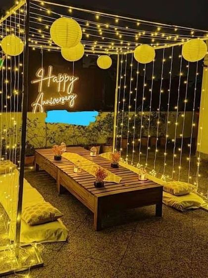 An anniversary celebration under the stars, with a fairy light cabana, low seating, and a "Happy Anniversary" neon sign.