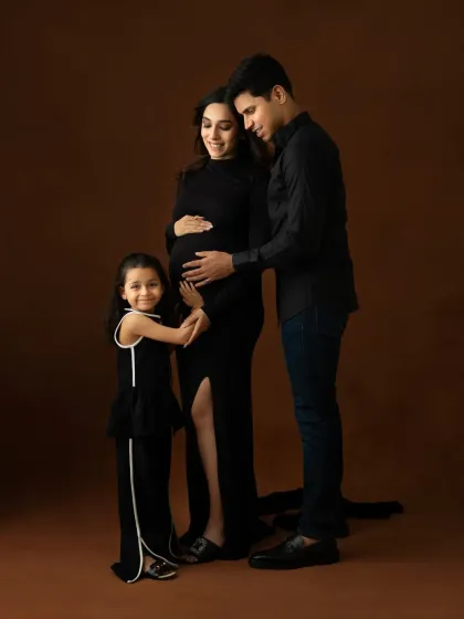 A beautiful family portrait with an expecting mother, father, and their daughter, all dressed in elegant black. This studio maternity photoshoot celebrates the growing family and the excitement of a new arrival.