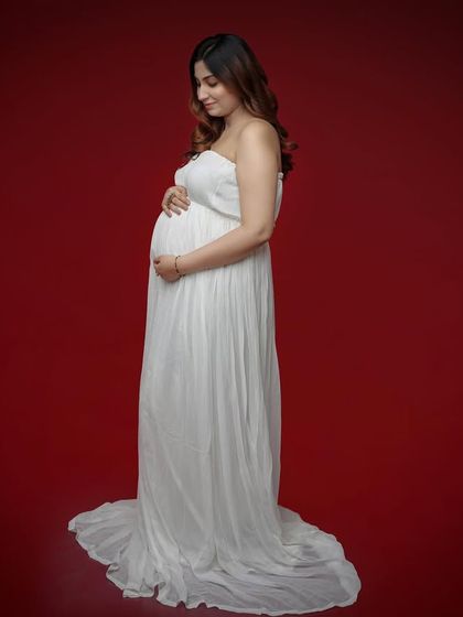 A simple and classic portrait against a solid red background. The white strapless gown provides a beautiful contrast, making the mom-to-be the sole focus.