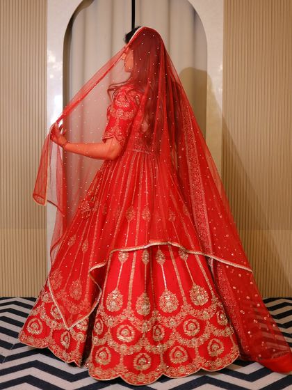 The back view of a classic red bridal lehenga with a sheer dupatta. The elegant fall of the veil and the detailed embroidery create a picture-perfect moment.