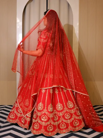 The back view of the red bridal lehenga, showing the beautiful drape of the dupatta. The sheer fabric adds a touch of grace without hiding the outfit.