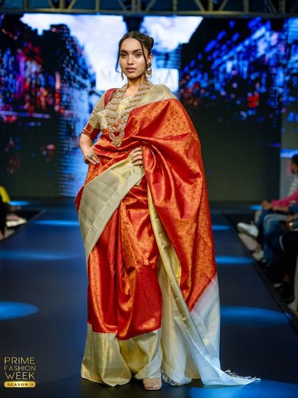 The model's confident pose highlights the dramatic flair of this red and off-white bridal saree.