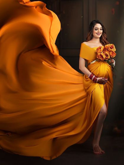 A vibrant and dynamic shot featuring a flowing mustard-yellow gown. The fabric is tossed to create a beautiful wave of color, and the client holds a matching bouquet of roses.