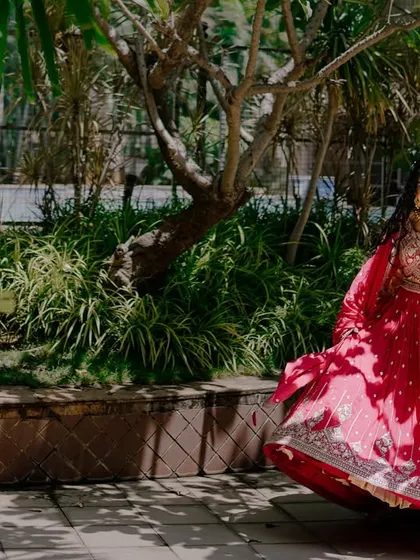 A joyful shot of the bride twirling in her red lehenga in a beautiful garden. This dynamic photo captures her happiness and the beauty of her bridal outfit in motion.