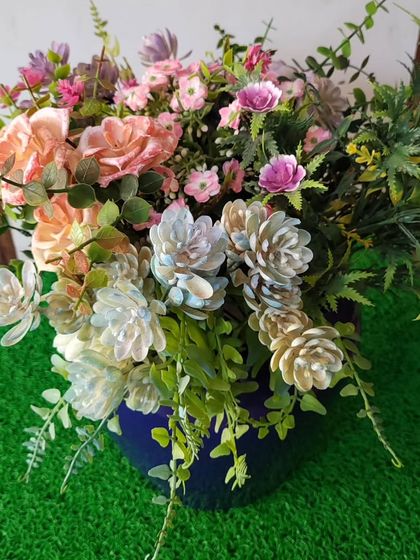 A lovely arrangement of mixed artificial flowers and greenery in a simple blue pot. This piece is designed to look lush and natural, adding a cheerful pop of color wherever it's placed.