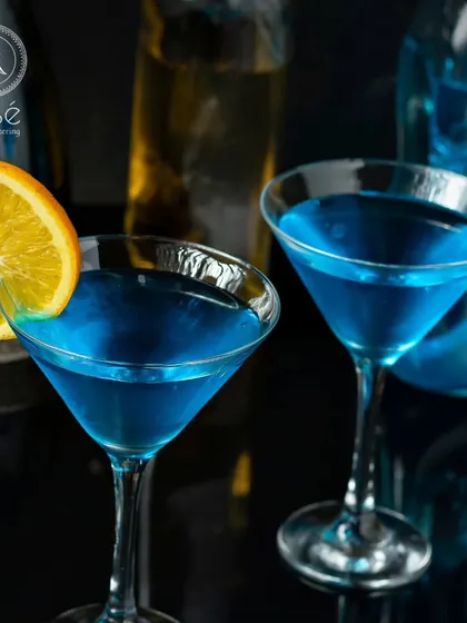 A vibrant blue cocktail, garnished with an orange slice and peel. This visually striking drink showcases our creativity and expertise in crafting unique beverages for your event's bar menu.