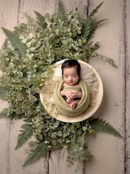 Nestled in nature. This overhead shot shows a newborn wrapped in green, surrounded by a wreath of fresh foliage, creating an earthy and beautiful image.