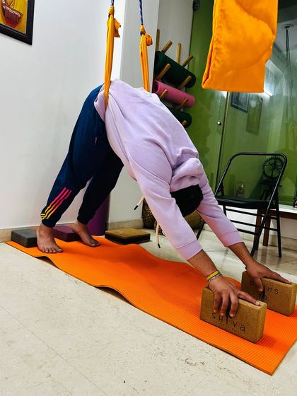 This student uses blocks and a yoga sling to work on a deeper version of Downward-Facing Dog. This setup helps to open the shoulders and lengthen the spine, preparing the body for more advanced poses.