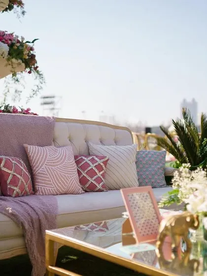 A chic lounge setup with a pastel pink and grey color scheme. The comfortable sofa is adorned with patterned cushions and a soft throw, creating an inviting space for guests to relax.