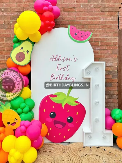 A "Tutti Frutti" first birthday party with colorful balloons and cute fruit cutouts like a strawberry, avocado, and pineapple.