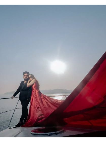 A dramatic sunset shot on a yacht in Goa. The bride's flowing red dress catches the light, creating a breathtaking and cinematic silhouette against the open sea.