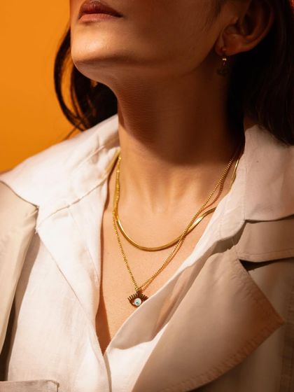 A close-up on a model wearing a layered gold necklace. The warm lighting and focus on the neck create an intimate and stylish shot.