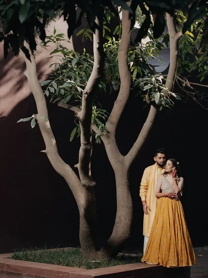 A quiet moment of togetherness. This pre-wedding shot captures the couple in a peaceful embrace against a dark wall and a beautifully shaped tree, creating a simple yet powerful composition.