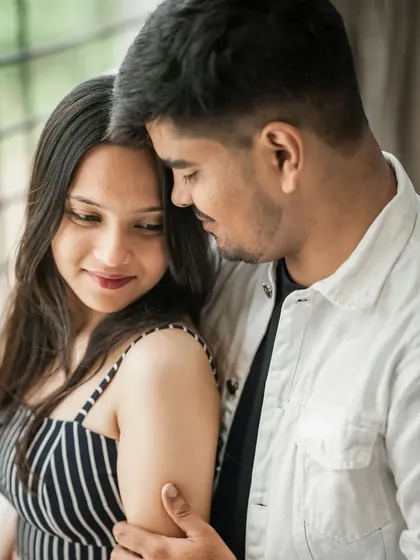 An intimate indoor pre-wedding photo, capturing a quiet moment of affection between the couple by a window.