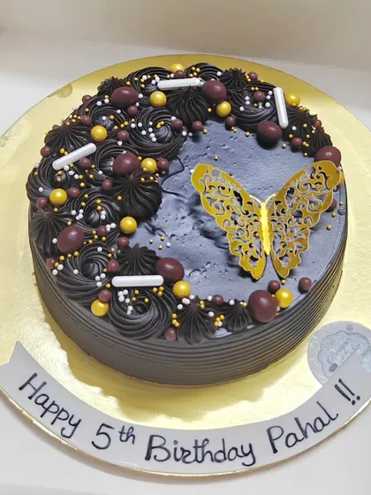 A dark chocolate cake with a golden butterfly accent. The contrast between the dark chocolate and the shiny butterfly creates a striking look.