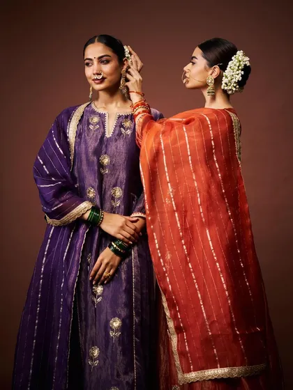 A moment of quiet preparation. This image captures two models in beautiful silk suits, one in royal purple and the other in a contrasting orange, getting ready for a celebration.