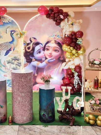 A divine Radha Krishna themed baby shower decoration, with beautiful backdrops and a maroon and gold balloon arrangement.