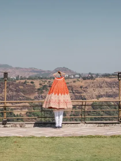 The bride's stunning orange lehenga hangs against the vast, mountainous landscape. This artistic shot creates a beautiful contrast and builds anticipation for her bridal look.
